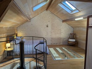 A loft bedroom with a sloped ceiling, skylights, a bed with striped bedding, a chair, and a small table with a lamp. - Secluded house with private pool and spa, Charente (Montignac-le-Coq)