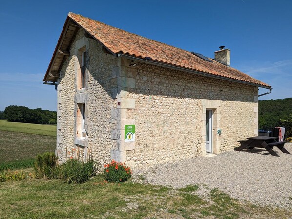 Un bâtiment en pierre avec un toit en tuiles, un petit porche et une enseigne indiquant qu’il s’agit d’un gîte.