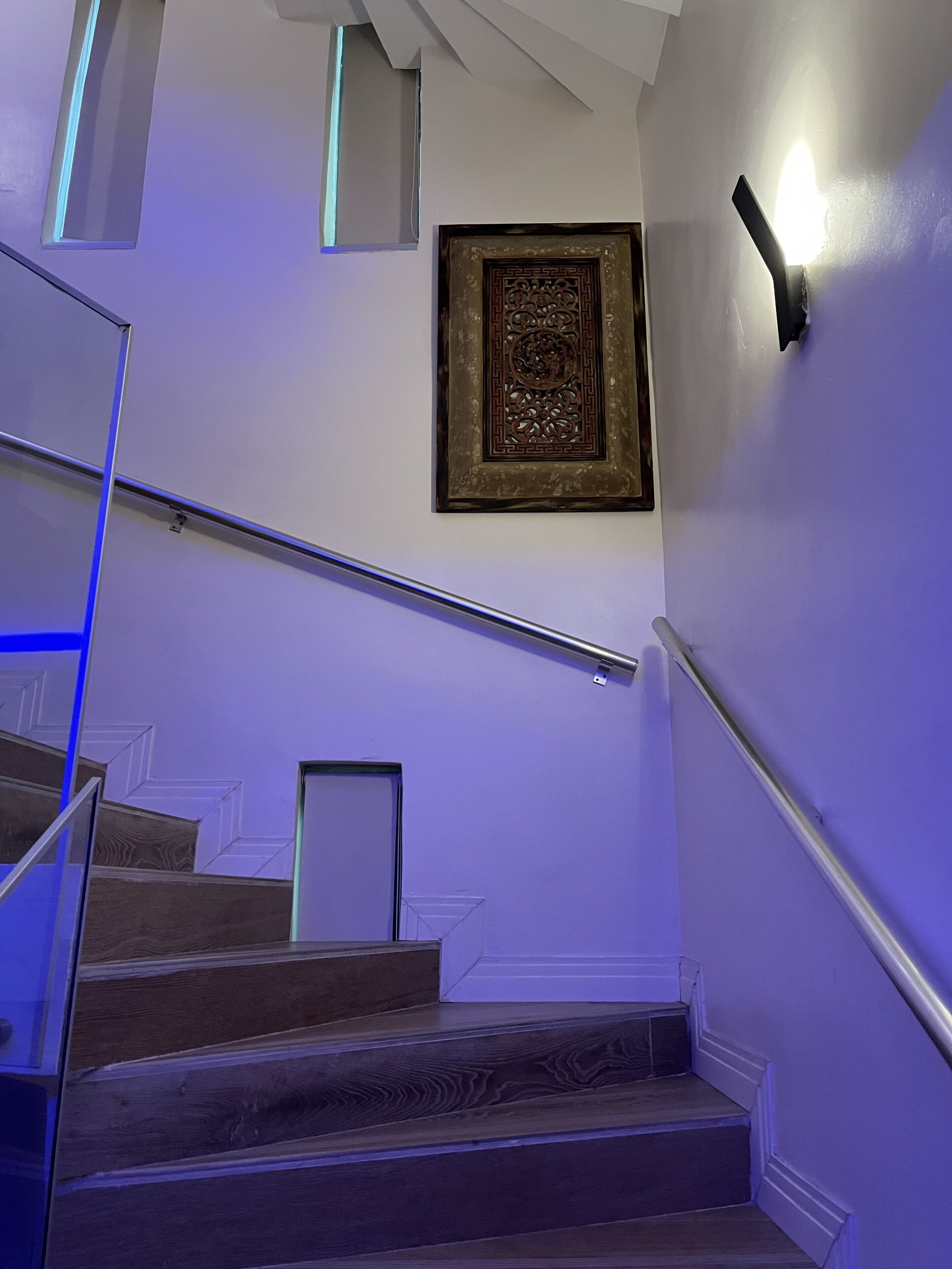 A staircase with a handrail, a wall-mounted light, and a framed artwork.