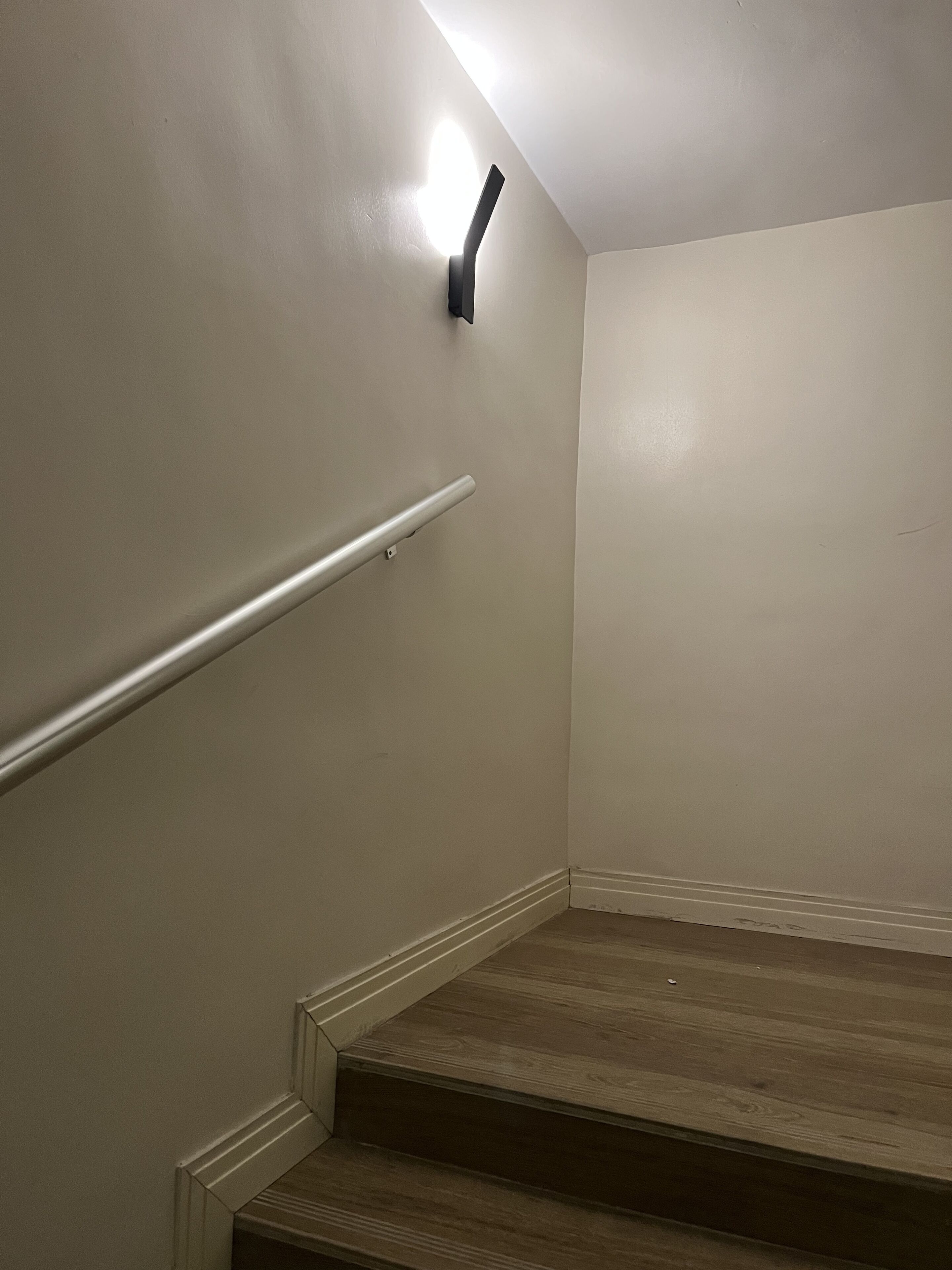 A staircase with a handrail and a light fixture on the wall.