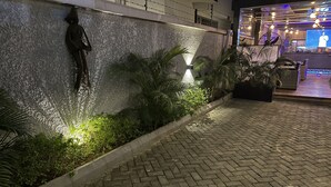A nighttime view of a hotel entrance with a stone wall, water feature, and outdoor seating area. - Riivana Leisure Tavern (Lekki)