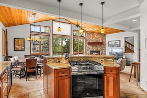 A modern kitchen with a central island, a stone accent wall, and large windows.