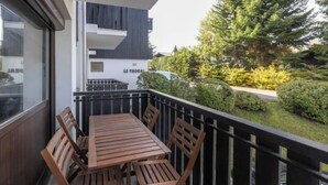 A balcony with a wooden table and chairs, a black railing, and a view of a residential area with trees and a building labeled "LE THORAL". - Appartement au Pied des Pistes (Arâches-la-Frasse)