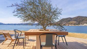 A wooden deck with a table and chairs, overlooking a body of water and hills.