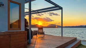 A wooden deck with a glass enclosure overlooking a lake at sunset. - Setouchi Hideaway Resort (Onomichi)