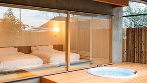 A modern room with a large sliding glass door leading to a balcony, a wooden floor, a small round bathtub, and a bed with white bedding. - Setouchi Hideaway Resort (Onomichi)