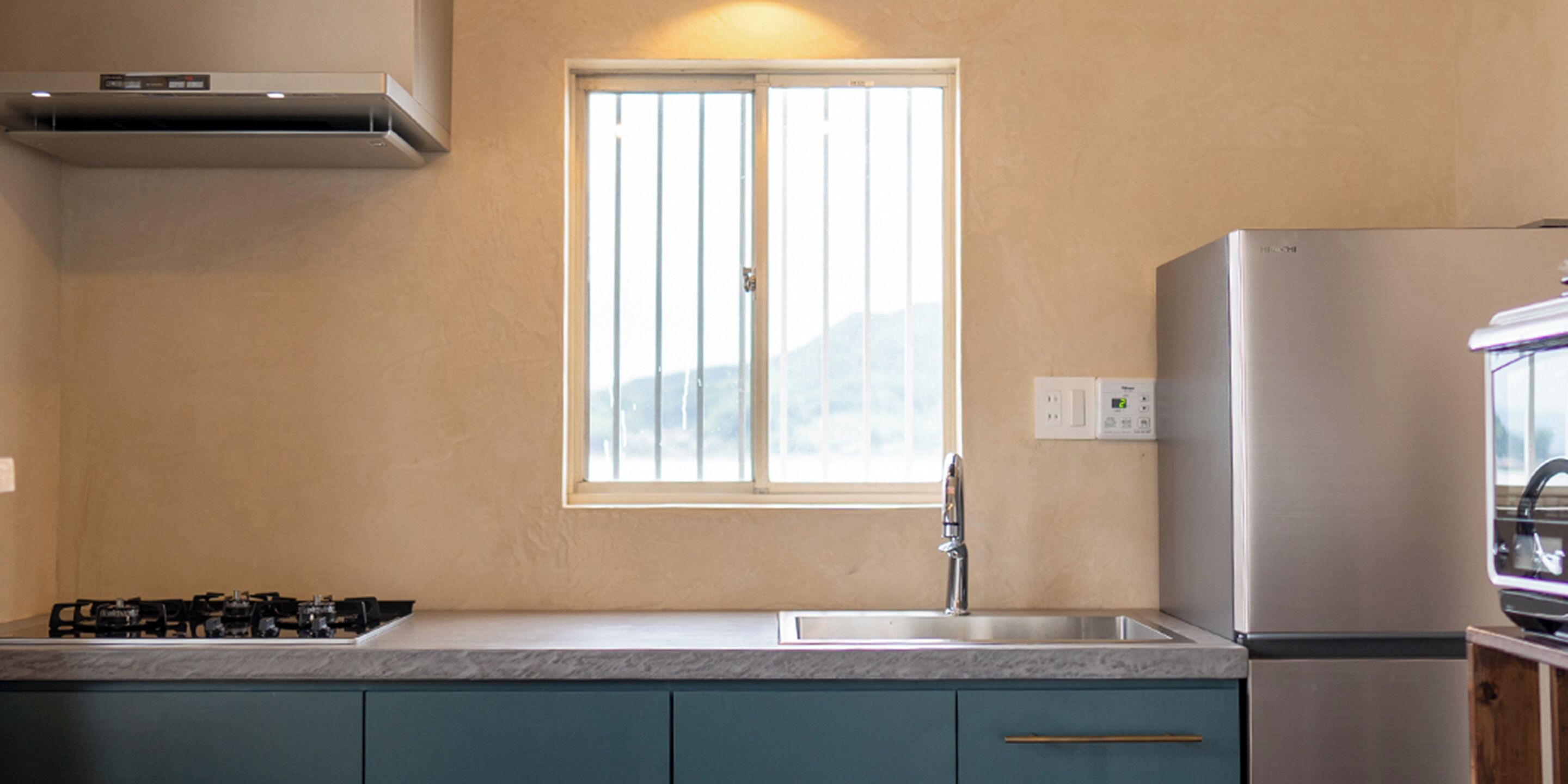 A kitchen with a gas stove, a stainless steel refrigerator, a window with blinds, and a sink.