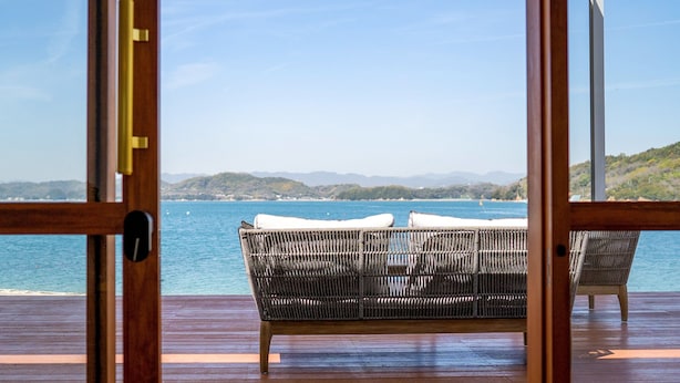 A wooden deck with a wicker chair and a view of the sea and mountains. - Setouchi Hideaway Resort (Onomichi)