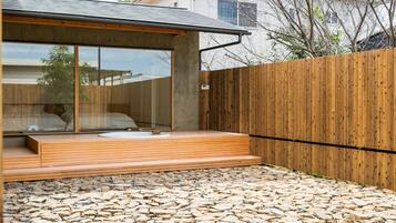 A modern outdoor bathroom with a stone-tiled floor, wooden deck, and a large window.