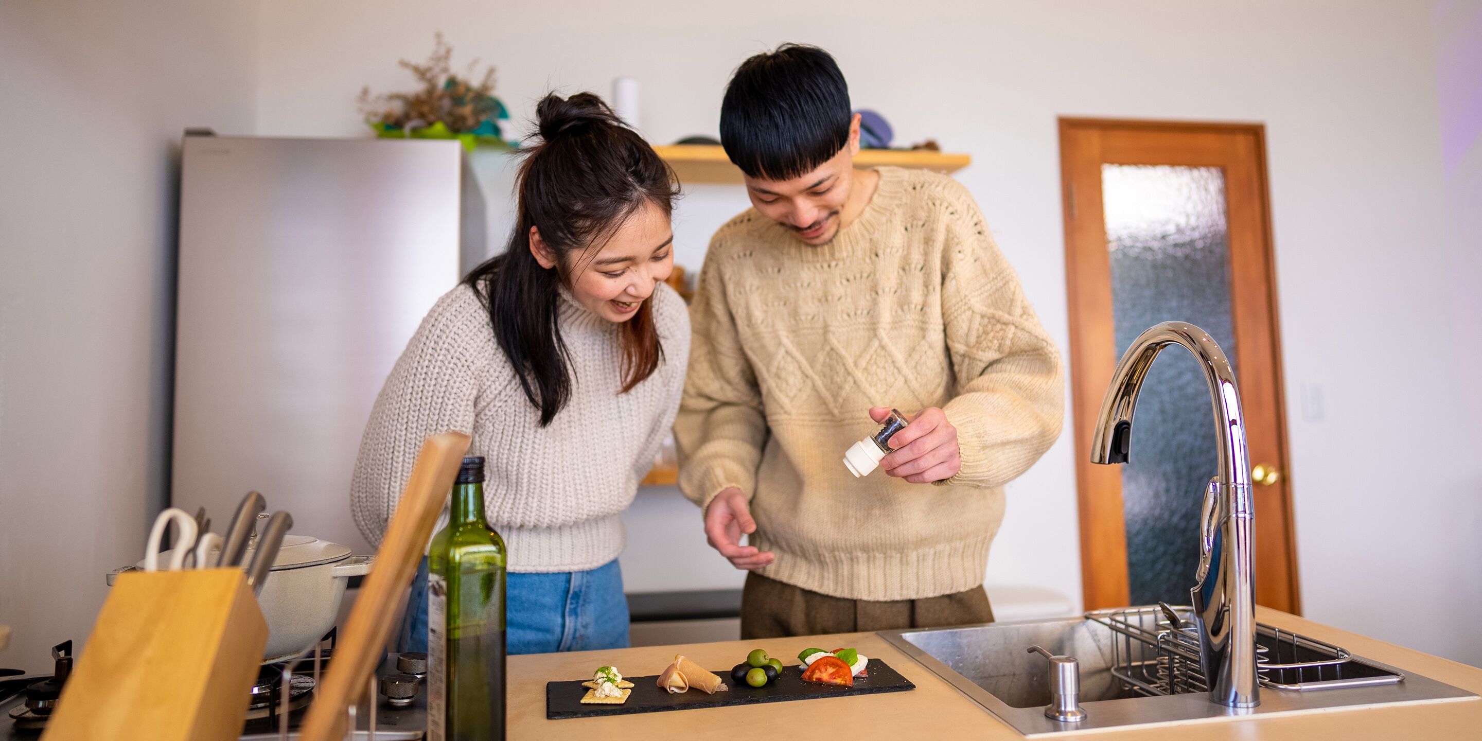 A kitchen with a sink, a cutting board with food, and a bottle of olive oil.