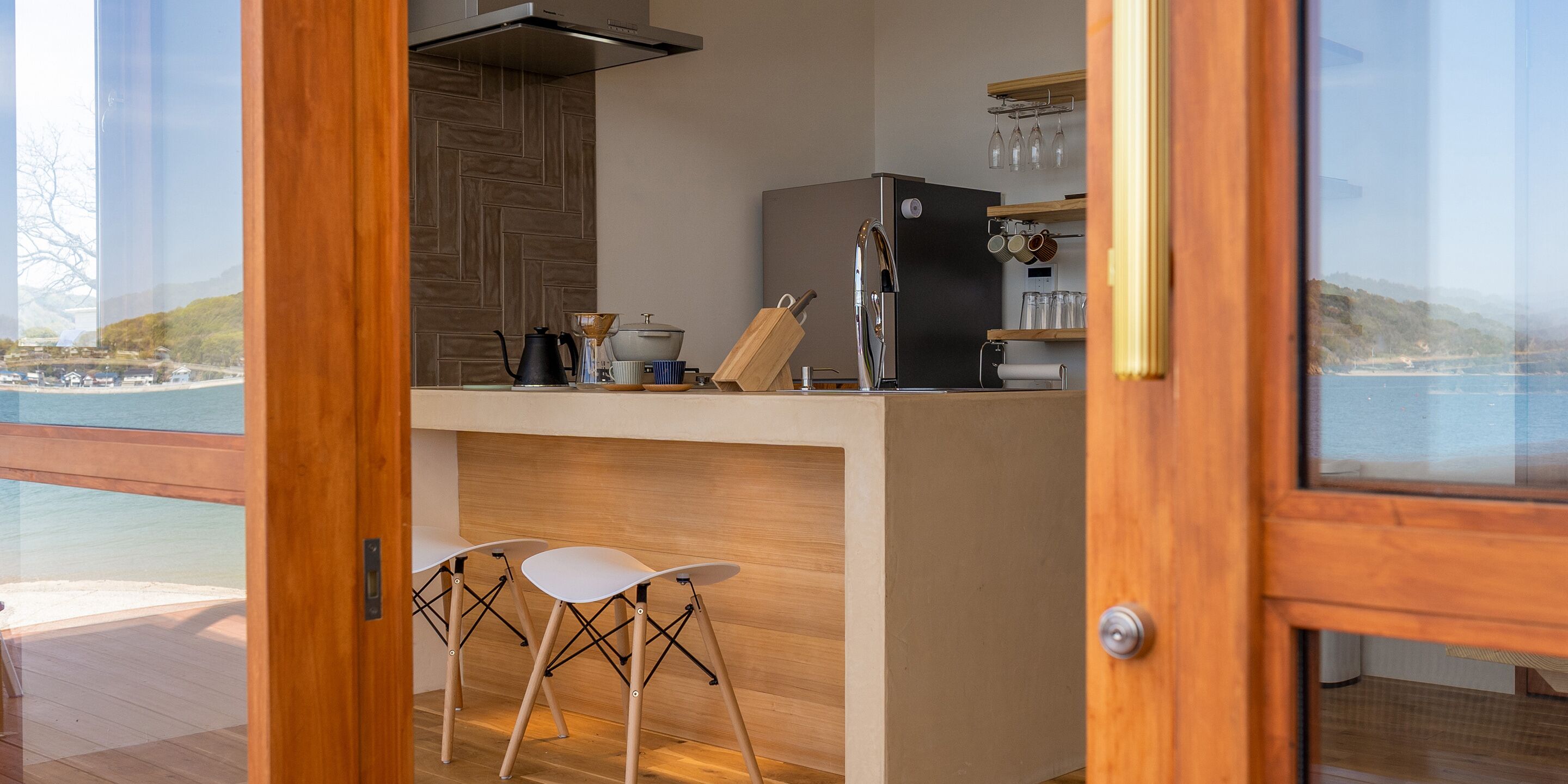 A modern kitchen with a view of the sea, wooden bar stools, and a stainless steel refrigerator.