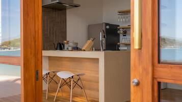 A modern kitchen with a view of the sea, wooden bar stools, and a stainless steel refrigerator.