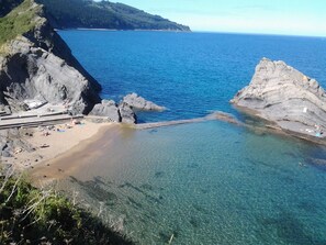 A coastal beach with clear water, rocky formations, and a sandy area with people. - Comfortable apartment in the center of Bermeo. (Bermeo)