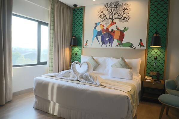 Une chambre d’hôtel avec un grand lit, une décoration en forme de cœur réalisée avec des serviettes, un tableau représentant des animaux aux couleurs vives et une vue sur l’extérieur.