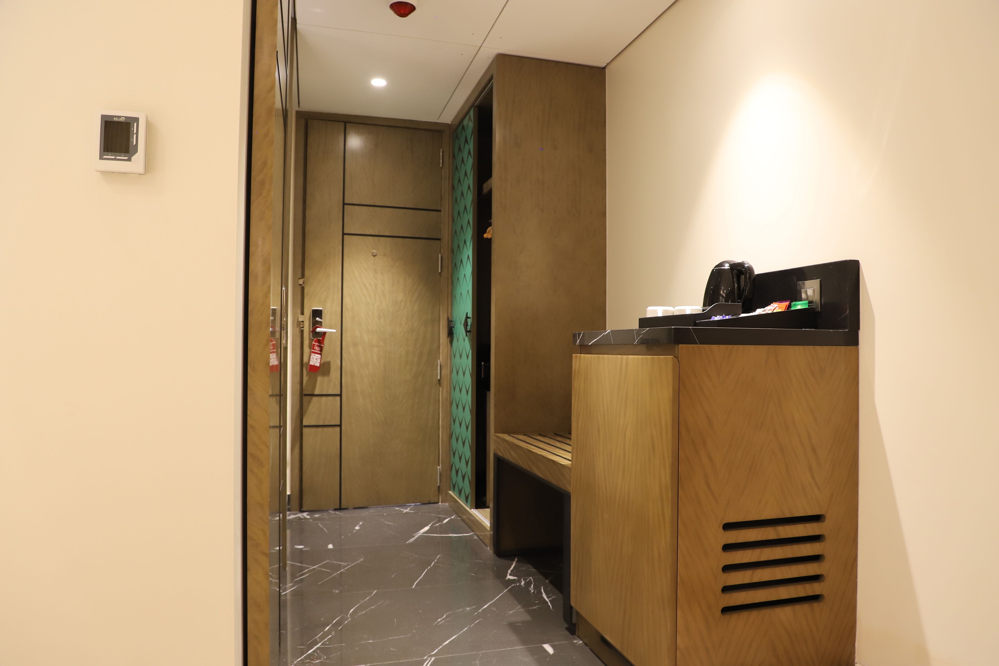 A hotel hallway with a reception desk, a fire extinguisher, and a door with a green patterned curtain.