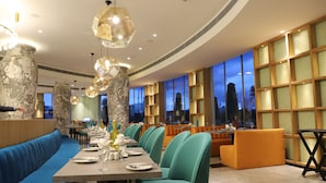 A restaurant with teal chairs, a long table set for dining, and a blue cushioned bench.