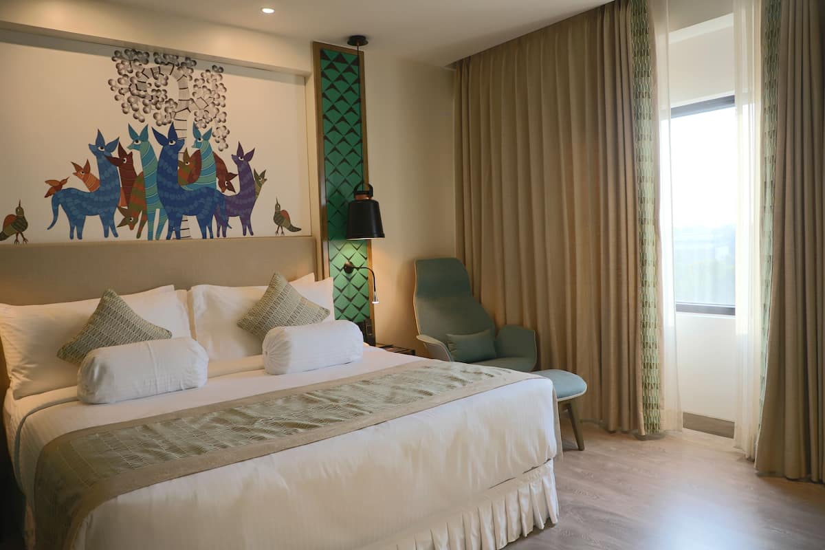 Habitación de hotel con una cama grande, una silla, una obra de arte en la pared y una ventana con cortinas.