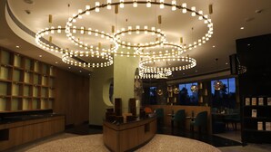 A modern hotel lobby with a curved reception desk, multiple seating areas, and a large, circular chandelier.