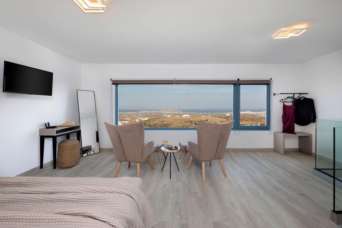 A modern hotel room with a large window, a flat-screen TV, a small table with chairs, and a bed.