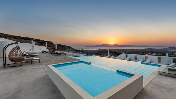 Una piscina a sfioro sul tetto con vista sul tramonto, sedie a sdraio e una sedia amaca.