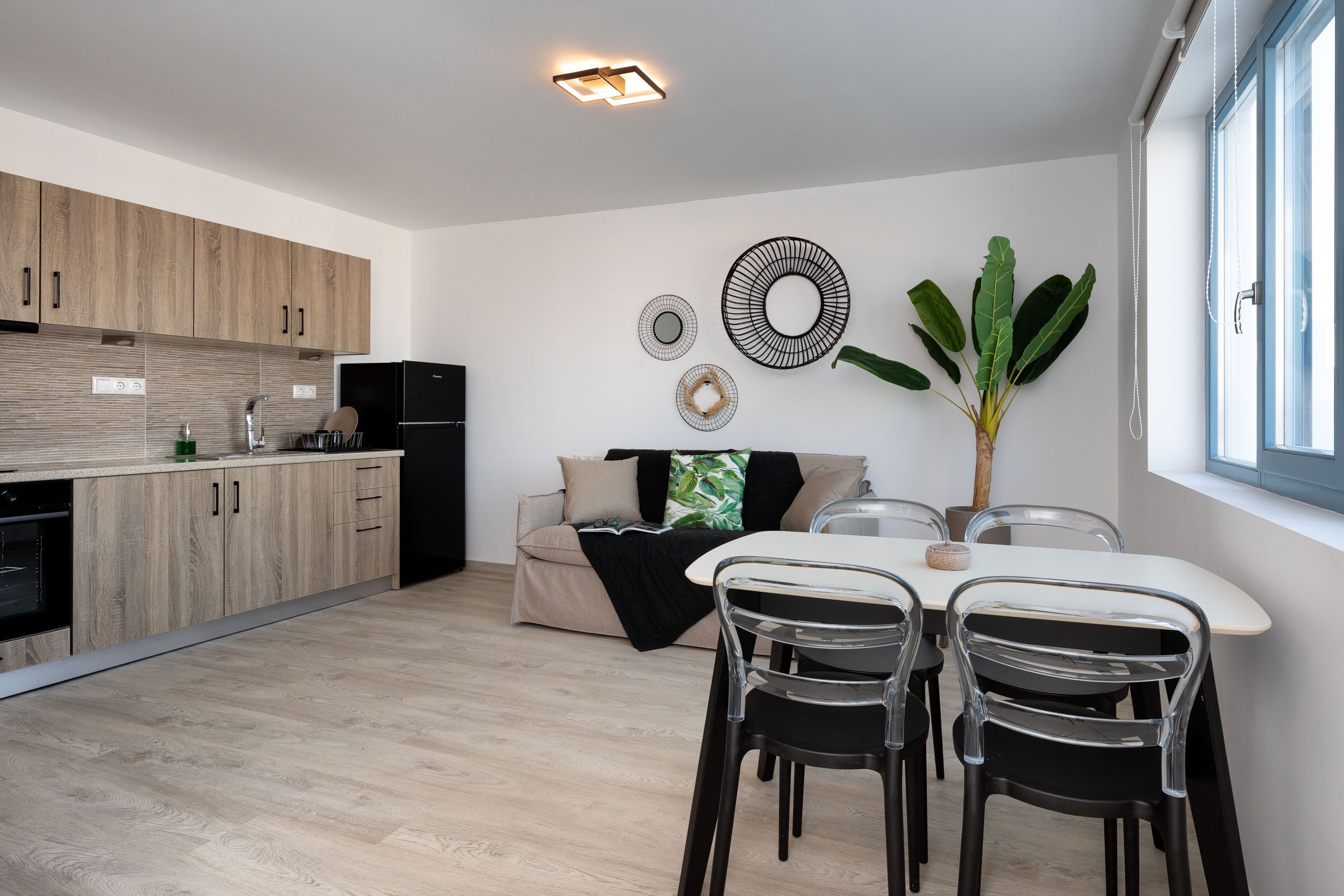 A modern kitchen with wooden cabinets, a dining area with a table and chairs, and a large plant.