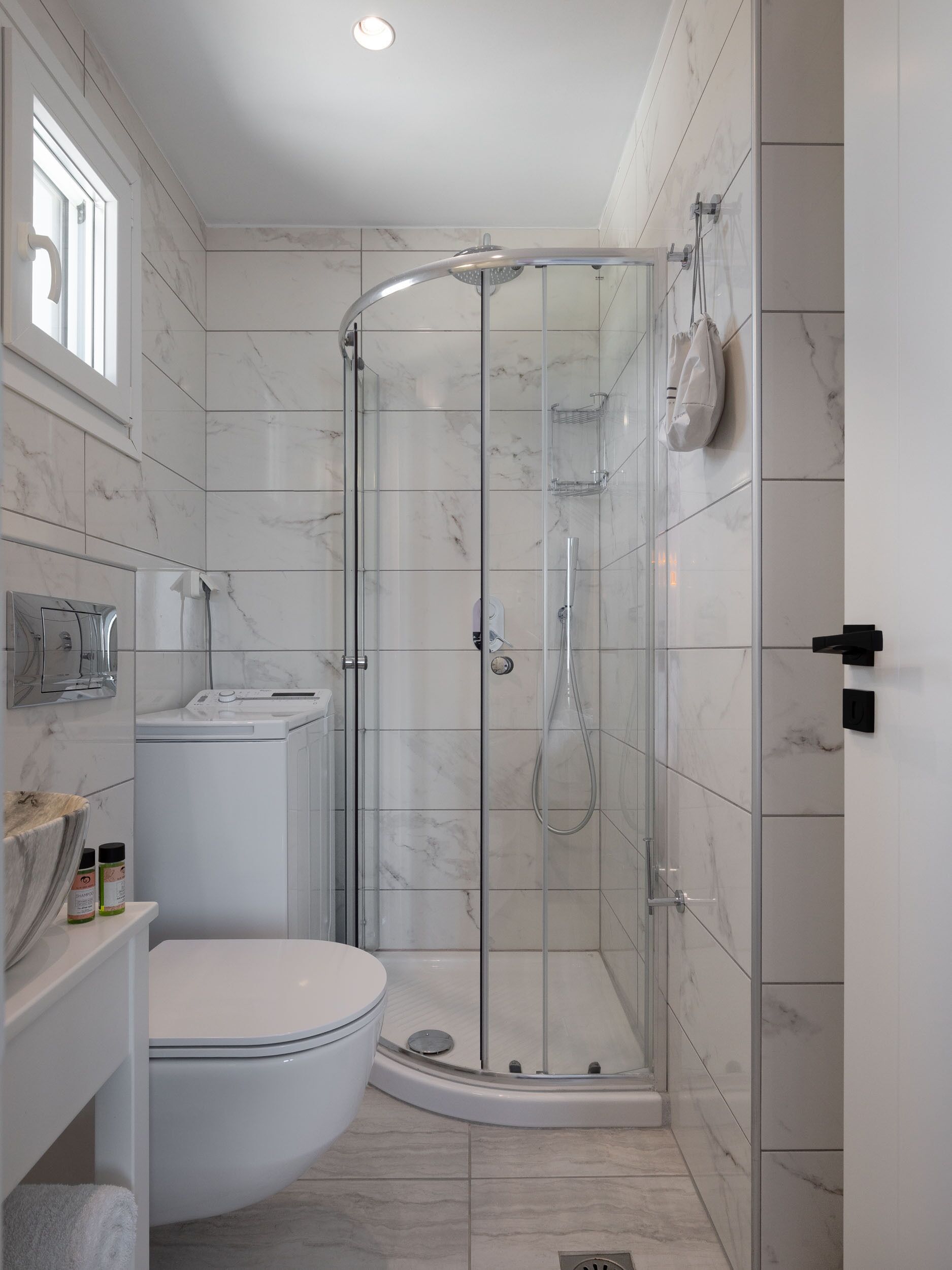 A modern bathroom with a glass-enclosed shower, a toilet, and a sink with a marble countertop.