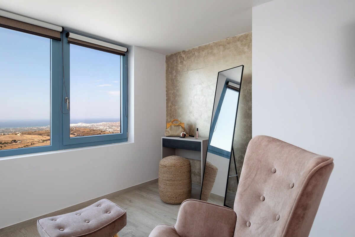 A modern room with a large window, a mirror, a cushioned bench, and a small ottoman.