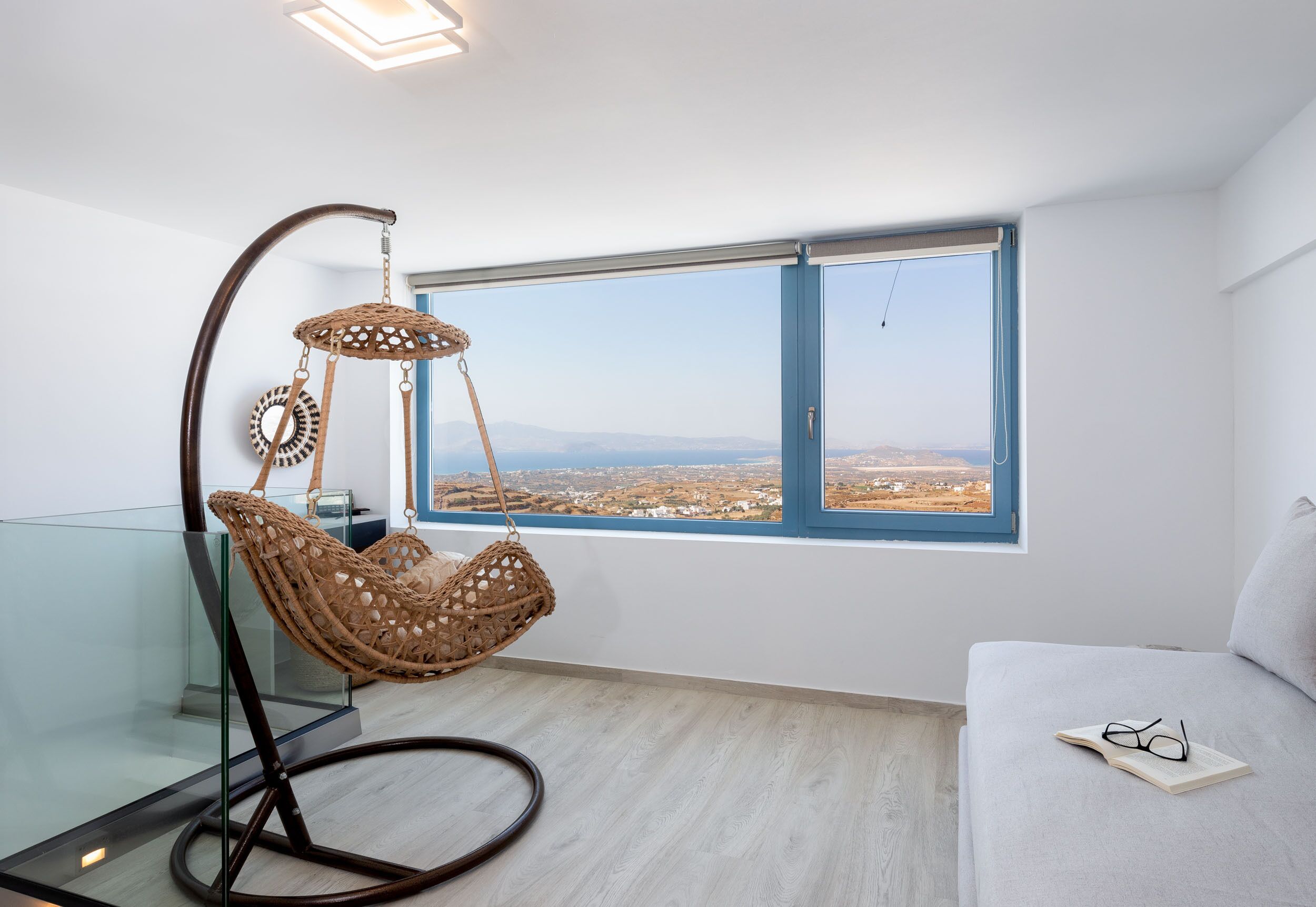 A modern room with a hanging chair, a sofa, and a large window offering a city view.