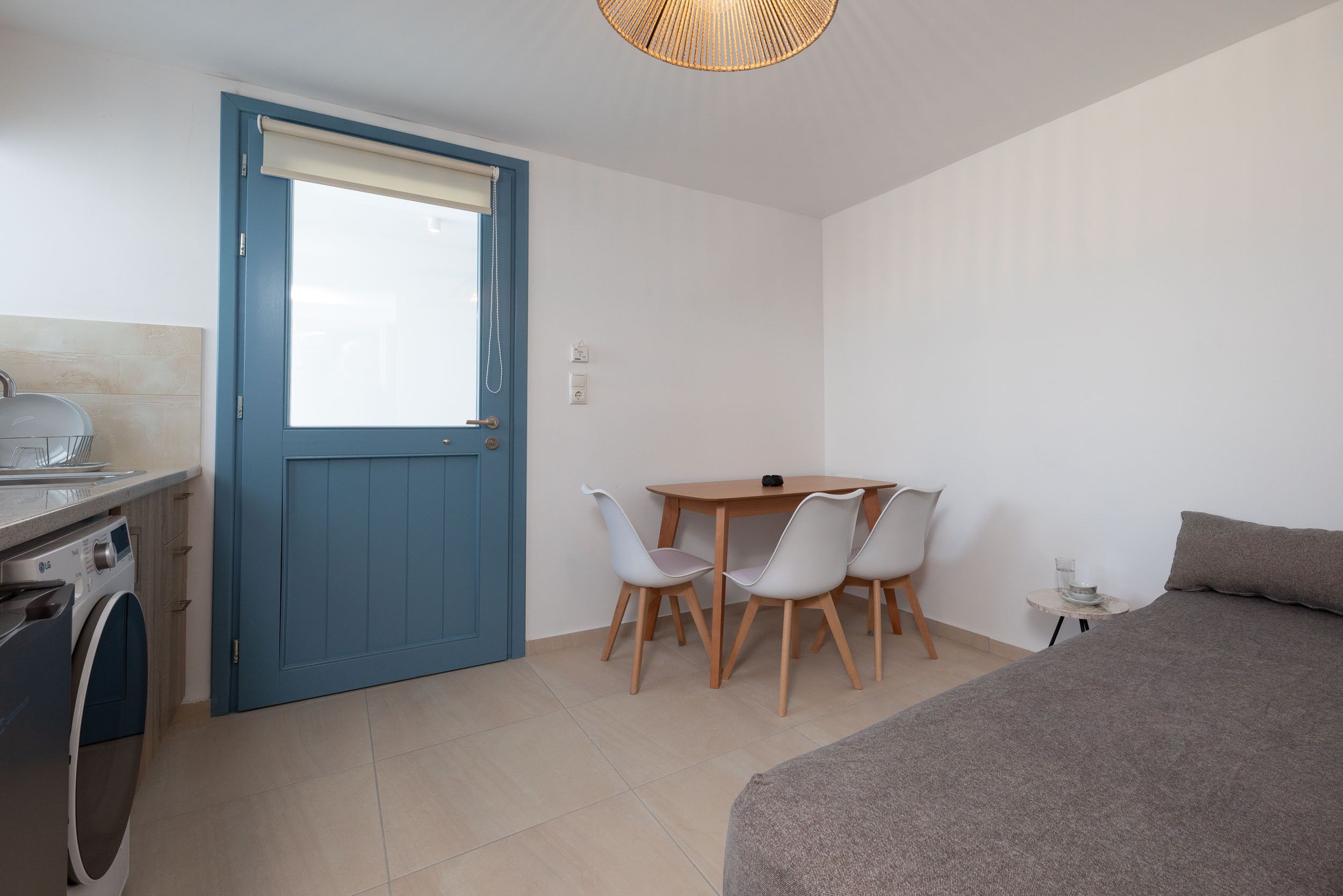 Une pièce de taille modeste comprenant un lave-linge, une table à manger avec des chaises, un lit et une petite table avec un plateau en verre.