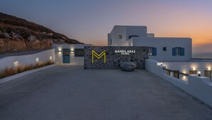 Un edificio moderno con facciata bianca, un muro in pietra con un grande logo 'M' e la scritta 'MANDILARAS VILLAGE' sulla parete.