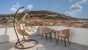 Una terrazza con un'amaca, due poltrone in vimini, un tavolino con un bicchiere di vino e vista su un pendio roccioso.