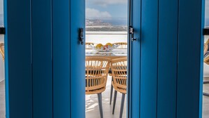 Una vista attraverso porte blu su un tavolo e sedie su una terrazza con una vista panoramica.