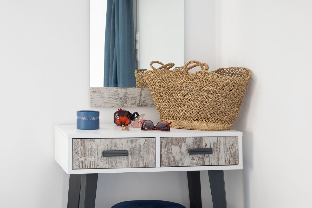 A bedroom with a white dresser, a woven basket, a blue cushion, and a TV mounted on the wall.