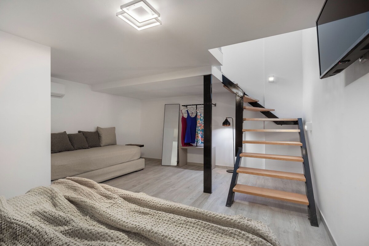 A modern living room with a sofa, a staircase, and a TV mounted on the wall.