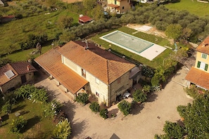 A stone building with a tiled roof, a paved courtyard, and a rectangular swimming pool.