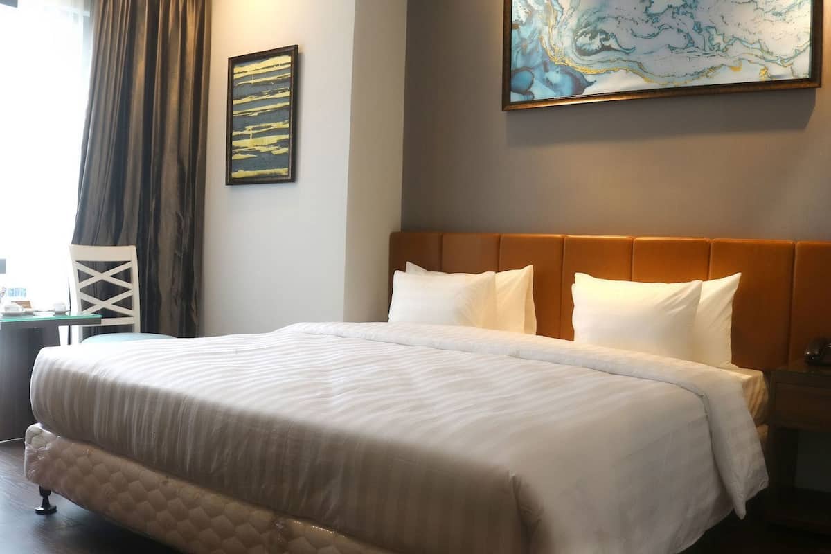A hotel room with a large bed, a headboard, a nightstand, a lamp, a painting on the wall, and a window with curtains.
