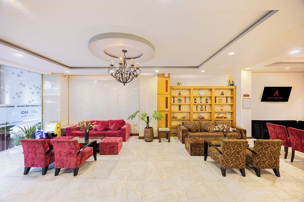 Eine Hotelhalle mit roten und braunen Sofas mit Muster, einer Kristallleuchtre, einem Holzregal und einem Fernseher an der Wand.