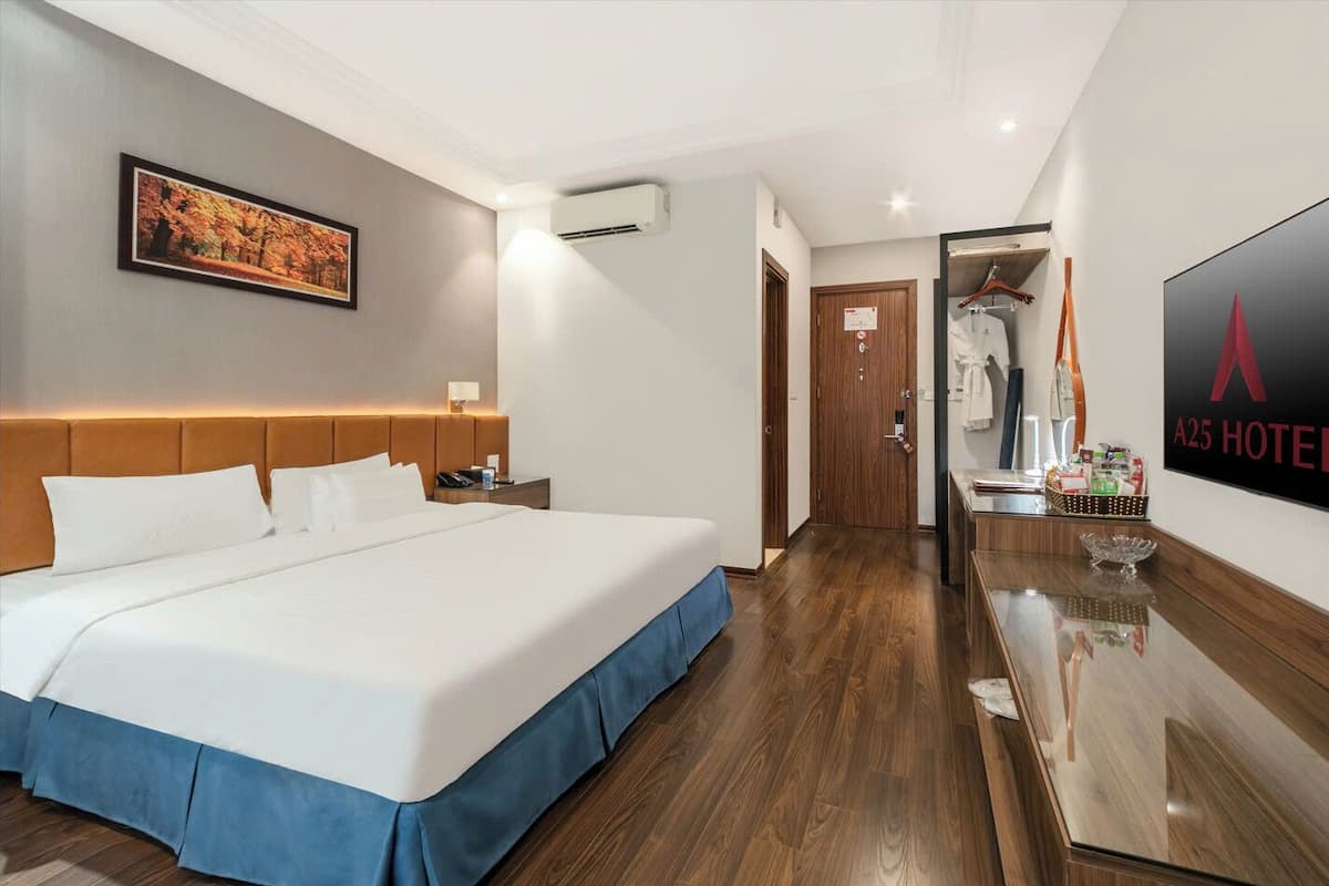 A hotel room with a large bed, a wooden headboard, a flat-screen TV, a wooden desk, and a wardrobe.