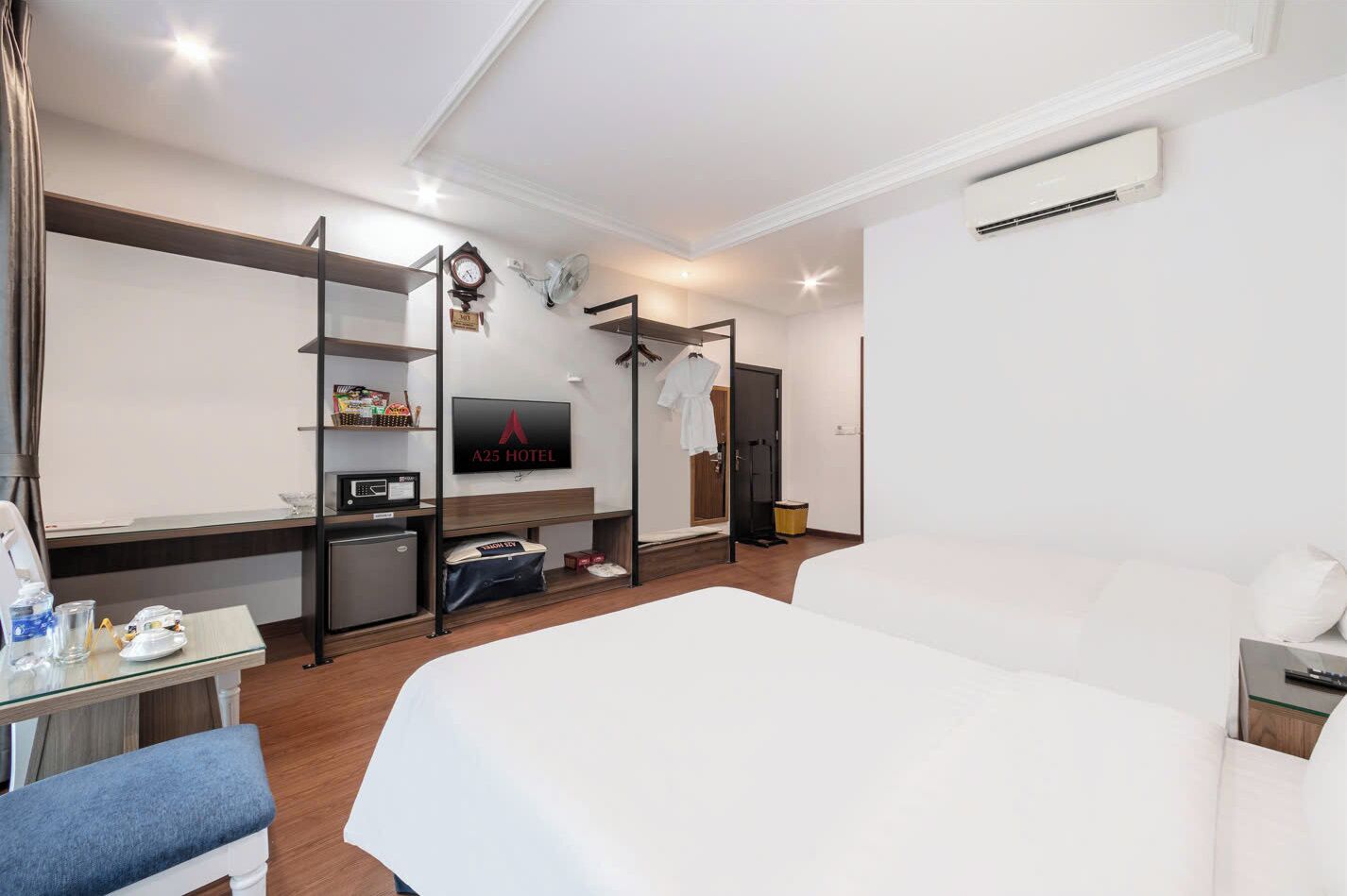 A hotel room with a bed, a TV, a desk with a computer, a mini-fridge, and a wardrobe.