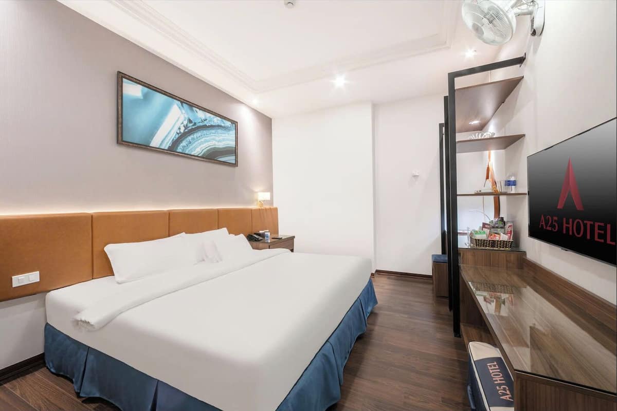 A hotel room with a large bed, a flat-screen TV, a desk with a basket, and a wall-mounted shelf.