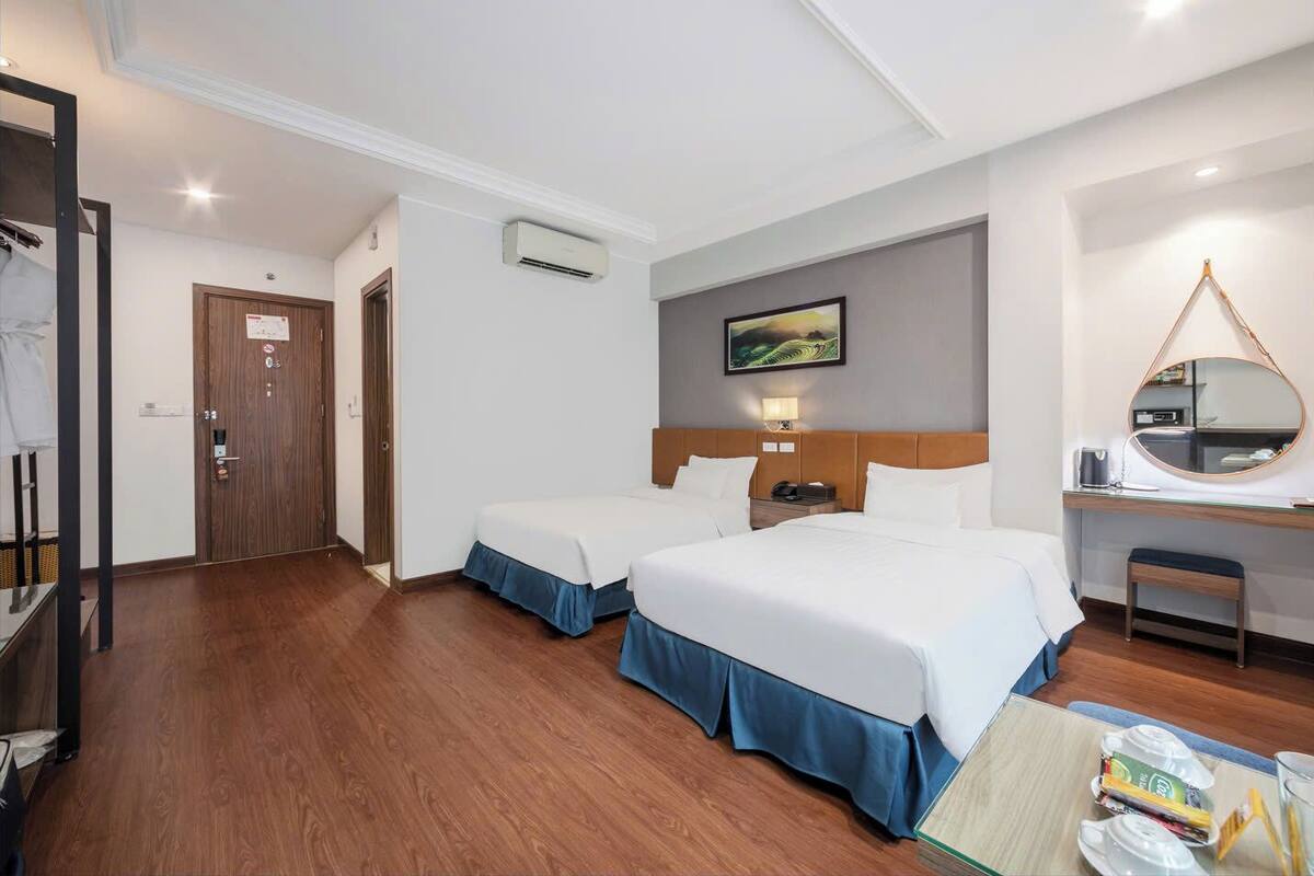 A hotel room with two beds, a desk, a chair, and a mirror.
