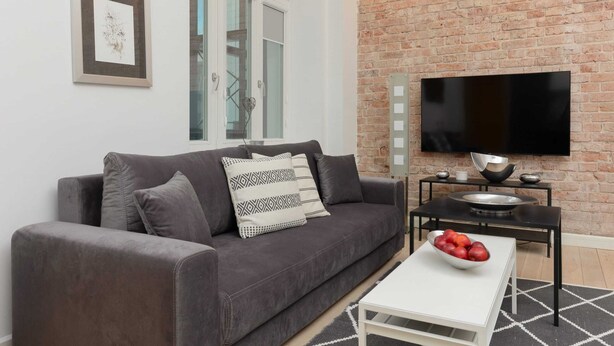 Un salon moderne avec un canapé gris, un téléviseur à écran plat et une petite table sur laquelle sont disposés des fruits.