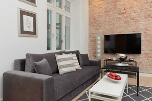 A modern living room with a grey sofa, a flat-screen TV, and a small table with fruit. - Sunny Apartment in Powiśle | Remote Work | Pets (Warszawa)