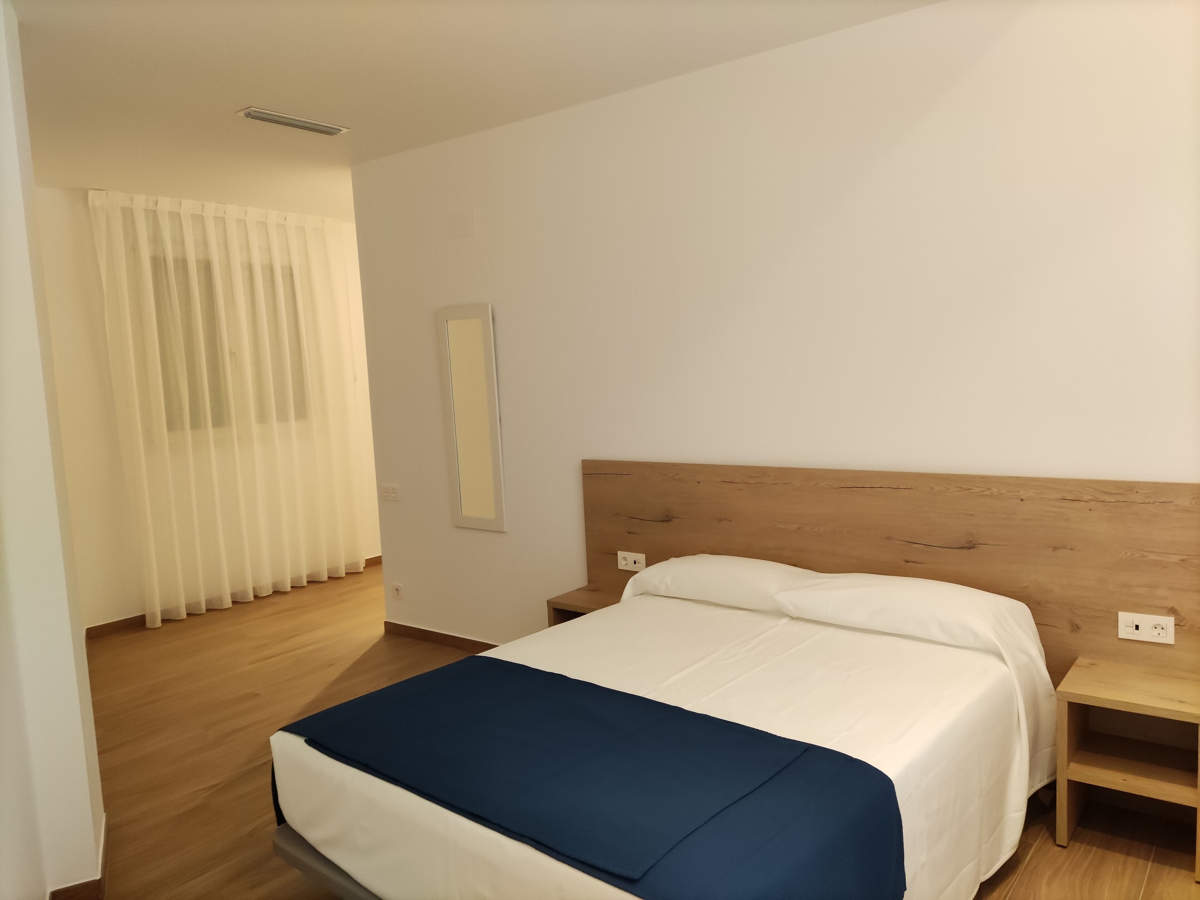 Ein Hotelzimmer mit Holz-Kopfteil, einem Bett mit weißer und blauer Bettwäsche, einem Nachttisch und einem Spiegel an der Wand.
