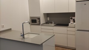 A modern kitchen with white cabinets, a built-in microwave, a refrigerator, and a large island with a sink. - IBERFLAT APARTAMENTOS TRINIDAD (Castelló de la Plana)