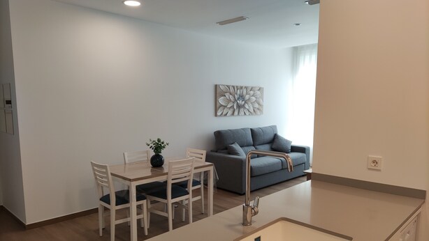 A modern kitchen with a central island, a dining area with a table and chairs, and a grey sofa against a white wall. - IBERFLAT APARTAMENTOS TRINIDAD (Castelló de la Plana)
