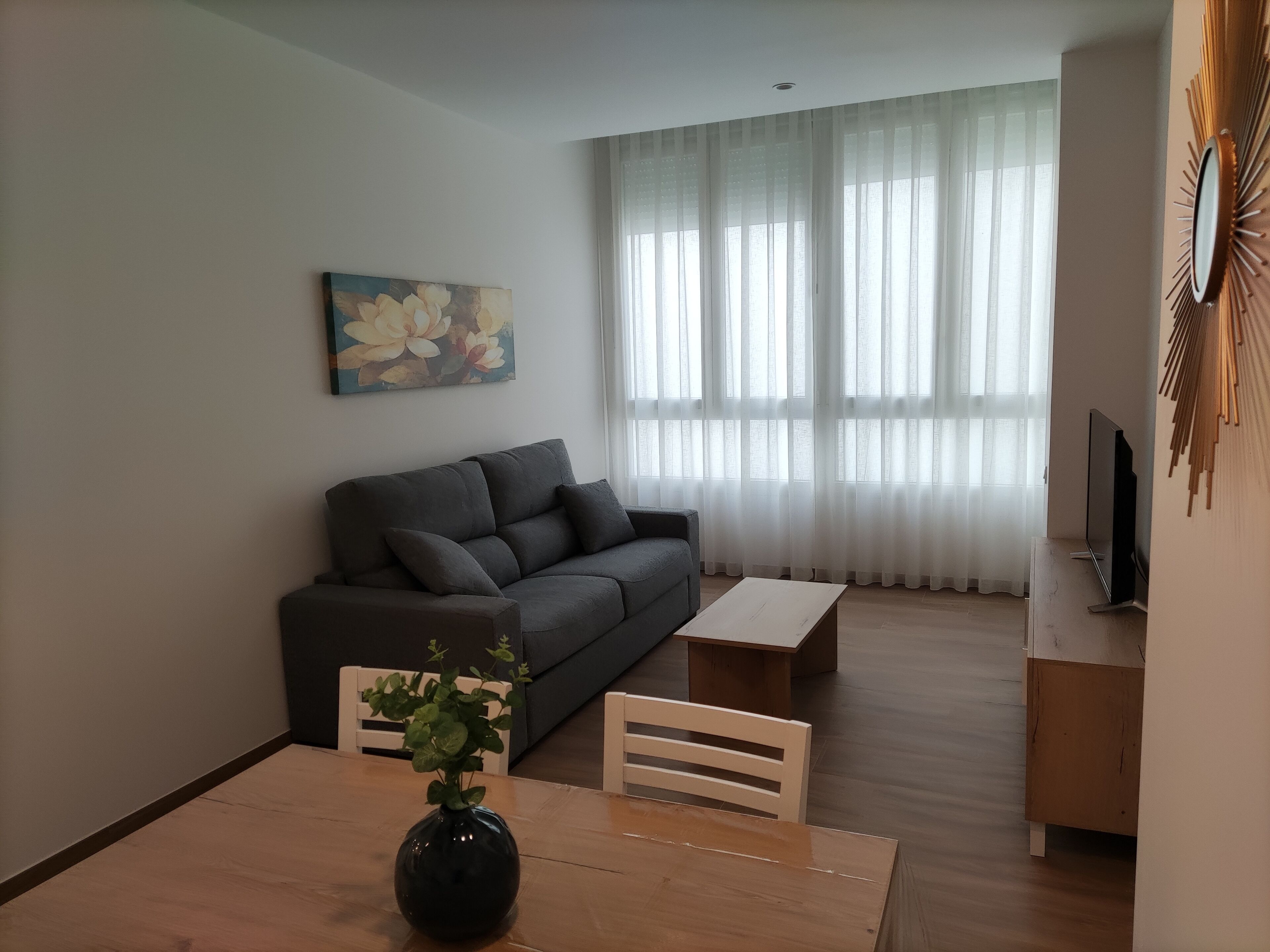 Een moderne woonkamer met een grijze bank, een houten eettafel en een tv-meubel.
