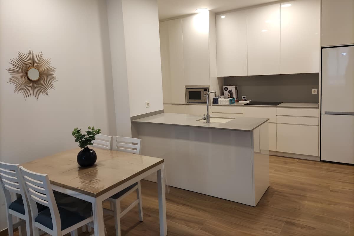 Eine moderne Küche mit weißen Schränken, einer zentralen Kochinsel mit Spüle und einem Essbereich mit Tisch und Stühlen.