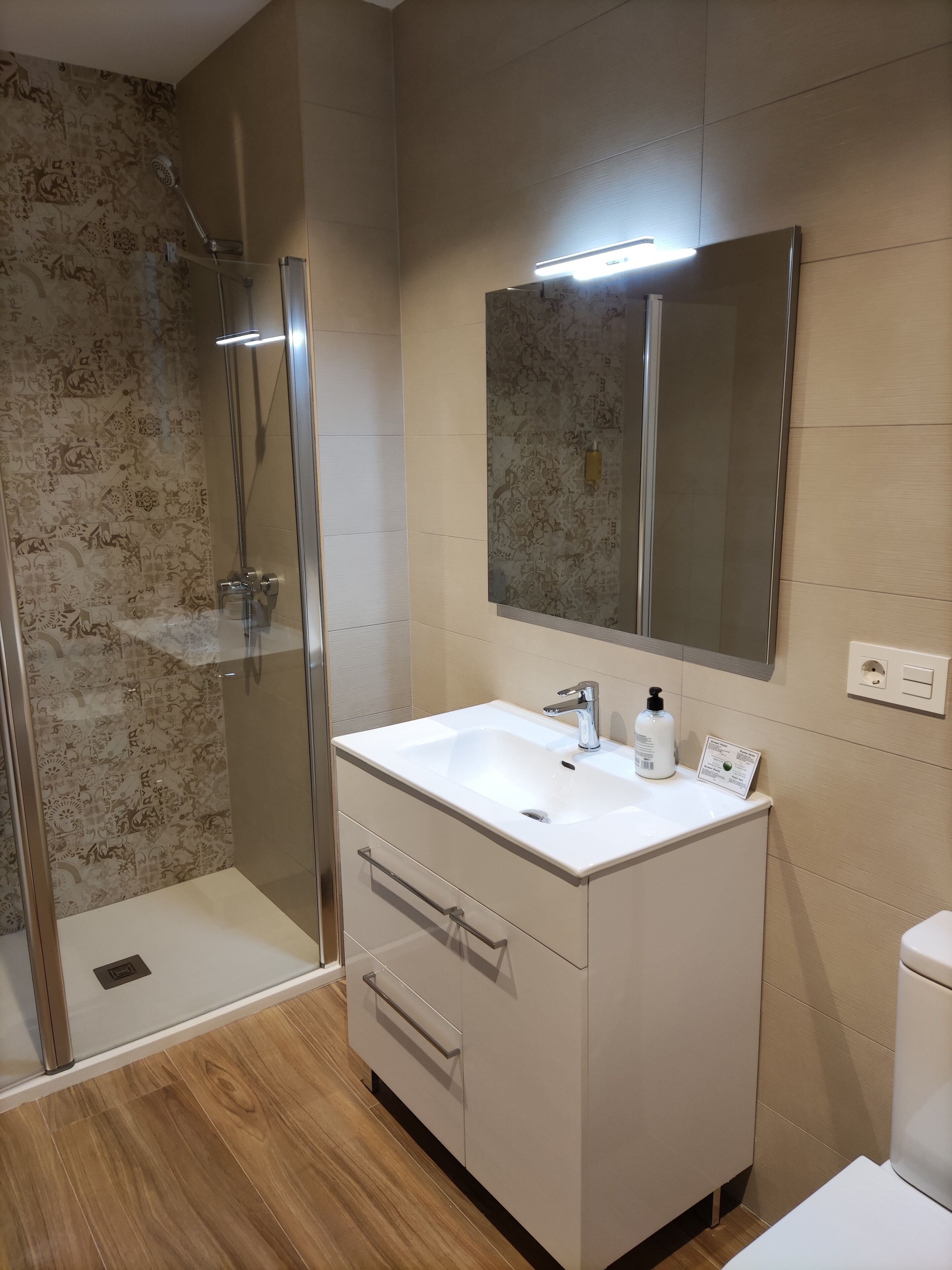 A modern bathroom with a glass shower enclosure, a white sink with a mirror above it, and a toilet.