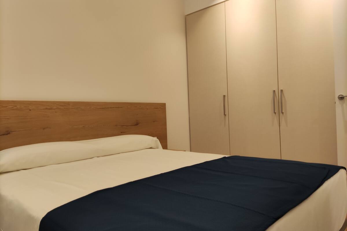 Ein Schlafzimmer mit hölzernem Kopfteil, einem Bett mit weißer und dunkelblauer Bettwäsche und einem zweitürigen Kleiderschrank.